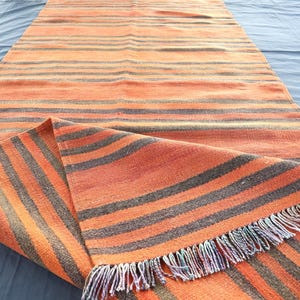 May include: A striped woven rug with orange and gray stripes and fringe on the edges.