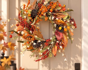 May include: A circular autumn wreath featuring a dense arrangement of orange and red berries, dark brown pinecones, and multicolored fall leaves in shades of yellow, brown, and red, accented with small white flowers on a twig base.