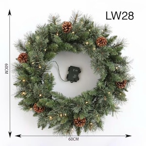 Puede incluir: Una corona navideña verde, de 60 cm de diámetro, adornada con piñas y pequeñas luces. La corona tiene una batería y el texto "LW28".