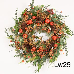 May include: A circular autumn wreath featuring a mix of foliage, including green leaves, orange berries, and small orange pumpkins. Pine cones are scattered throughout the wreath. The text "Lw25" is visible in the lower right corner.