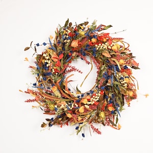 Peut inclure: Une couronne circulaire composée d'éléments botaniques séchés dans une palette vibrante de rouge, bleu, jaune et vert. L'arrangement présente de longues feuilles fines, de petites grappes de baies blanches et divers brins floraux séchés.