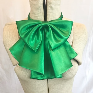 May include: A large, green satin bow with multiple layers. The bow is tied around a mannequin's neck.