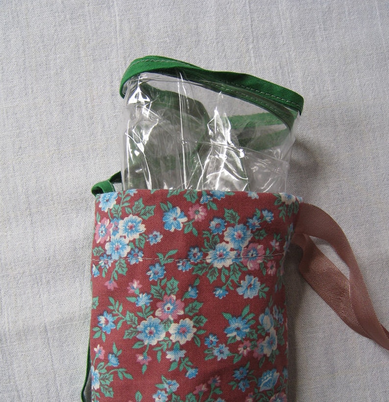 May include: A red fabric drawstring bag with a floral print and a clear plastic zippered pouch inside. The bag has brown ribbon ties.