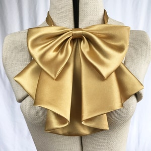 May include: A large gold satin bow tie with multiple layers and a ruffled design.