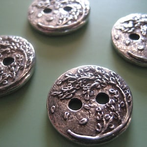 May include: Four round silver-toned metal buttons featuring a raised, textured relief design of a tree with branches and leaves. Each button has two central holes for attachment, with a polished finish and darkened recessed areas for contrast.