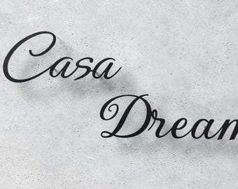 Pode incluir: As palavras "Casa Dream" estão escritas em cursivo preto elegante sobre um fundo cinza claro salpicado. O texto está ligeiramente inclinado, com "Casa" acima de "Dream".
