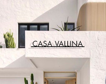 Pode incluir: Uma casa moderna branca com uma porta de madeira e uma placa que diz "Casa Vallina".