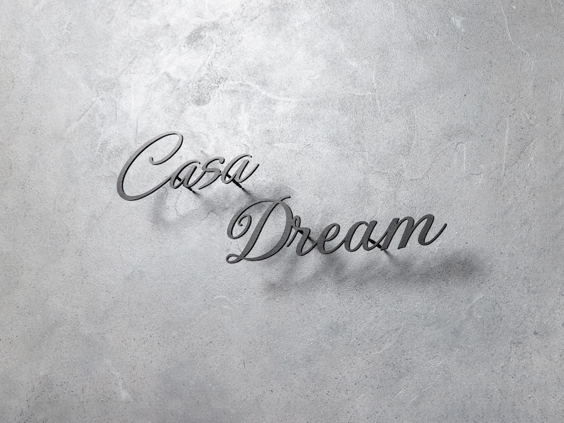 May include: Dark gray metal wall art spelling "Casa Dream" in a cursive font. The letters cast a shadow on the textured, light gray background. The art piece is suitable for home decor.