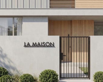 Pode incluir: Vista exterior de uma casa moderna com design minimalista. A fachada apresenta uma combinação de cinza claro e painéis de madeira. Um portão de metal preto e o texto "LA MAISON" são visíveis em frente à entrada.