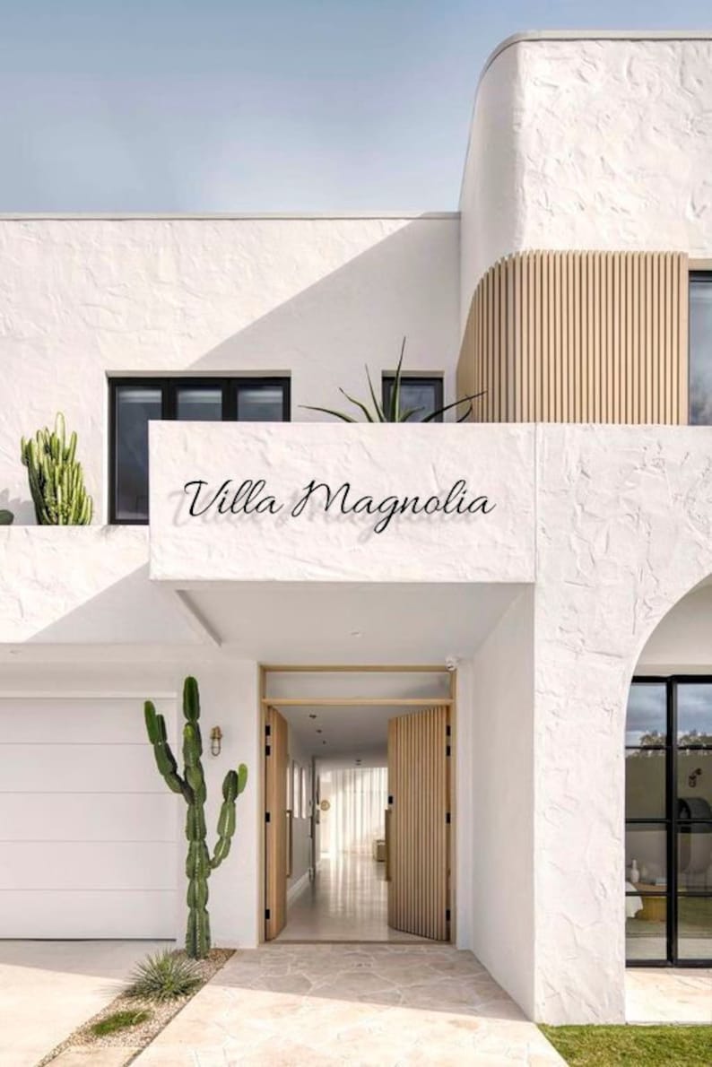 Pu&ograve; includere: Una casa moderna bianca con una porta in legno e le parole "Villa Magnolia" sopra la porta.