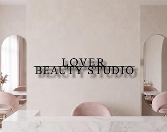 May include: A black metal wall sign featuring the text LOVER BEAUTY STUDIO in a bold, sans-serif font. The word LOVER is positioned above a horizontal line, while the words BEAUTY STUDIO are positioned below the same horizontal line.