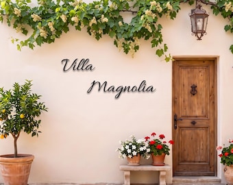 May include: A beige wall features the black text Villa Magnolia, a wooden door with a metal knocker, a lemon tree in a terracotta pot, a stone bench with two potted plants, and a hanging lantern under a green vine with small white flowers.