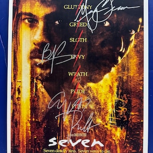 May include: A movie poster for the film "Seven" featuring Brad Pitt and Morgan Freeman. The poster has a dark, ominous color scheme with the actors' faces and signatures. The film's title and tagline are also visible.