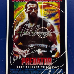 Puede incluir: Un cartel de la película "Predator" con Arnold Schwarzenegger. El cartel tiene el título "SCHWARZENEGGER" en la parte superior y "PREDATOR" en rojo. El texto en el cartel dice: "Nada como esto ha existido en la Tierra. Vino por la emoción de la caza. Eligió al hombre equivocado para cazar."