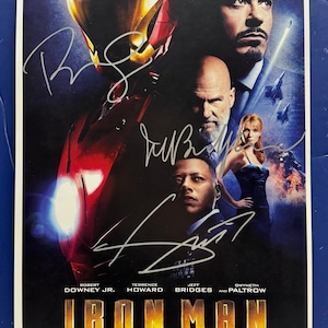 Peut inclure: Affiche du film Iron Man avec Robert Downey Jr., Terrence Howard, Jeff Bridges et Gwyneth Paltrow. L'affiche présente des signatures et le titre du film en lettres dorées. La date de sortie est le 5.2.08.