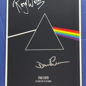 Puede incluir: Una portada de álbum negra con el diseño "Dark Side of the Moon" de Pink Floyd. Presenta un triángulo blanco, un arcoíris y las firmas de Roger Waters y David Gilmour.
