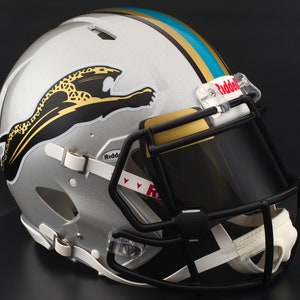 May include: Silver football helmet with a black facemask and a gold and teal stripe. The helmet features a leaping jaguar logo in black and gold. The visor is black and the helmet is made by Riddell.