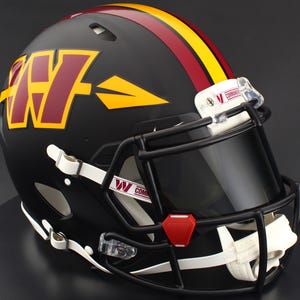 May include: A matte black football helmet featuring a large burgundy and gold W logo with an arrow design on the side. A central burgundy and gold stripe runs over the top. It includes a black face mask, a tinted visor, and white chin straps.
