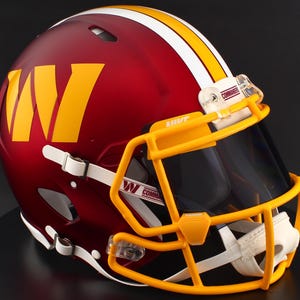 May include: A burgundy football helmet with a yellow and white stripe and a yellow facemask. The helmet features a large yellow "W" logo on the side and the word "Commanders" on the visor.