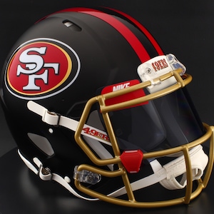 May include: A black football helmet with red and gold accents. The helmet features the San Francisco 49ers logo on the side and a red stripe down the center. The face mask is gold, and the visor is dark.