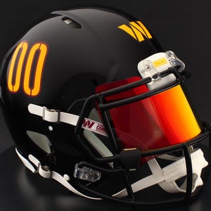 May include: A black football helmet with the number "00" in gold and burgundy on the side. The helmet has a gold "W" logo and a red-orange visor. The face mask is black, and the chin strap is white.