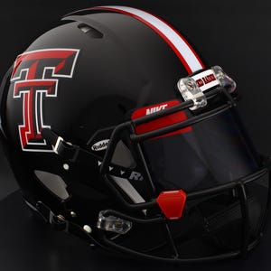 Puede incluir: Un casco de fútbol americano negro con una franja roja y blanca y el logotipo de los Red Raiders de Texas Tech. El casco tiene una máscara facial negra y una visera tintada. Las palabras "Red Raiders" son visibles en el clip de la visera.
