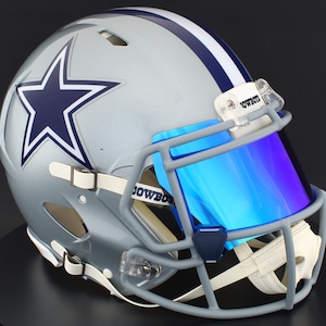 May include: Silver football helmet with a blue star logo and a blue and white stripe. The helmet has a blue visor and a gray facemask. The word "Cowboys" is visible on the visor clip.