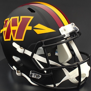 May include: A black American football helmet featuring a maroon and gold logo and stripes. The helmet has a black faceguard and white chin strap. The logo is a stylized "W" with a gold arrow.