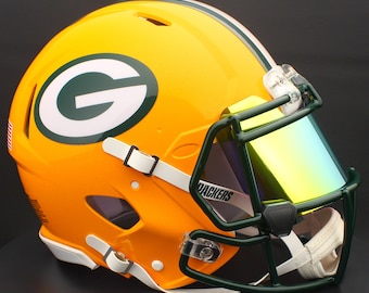 May include: A vibrant yellow football helmet with a green and white logo. The helmet features a green face mask and a tinted visor. The word "PACKERS" is visible on the visor. White chin strap and a stripe down the center.
