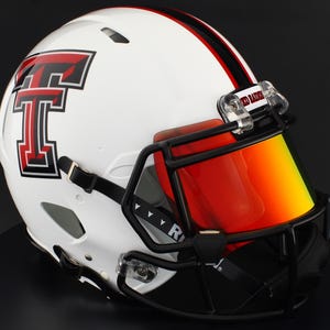 Puede incluir: Casco de fútbol americano blanco con un logotipo rojo y negro y una visera roja. El casco tiene una máscara facial negra y una correa negra. El casco tiene una raya roja en el centro.