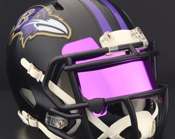 May include: A black football helmet with purple and white accents. The helmet features the Baltimore Ravens logo on the side and a purple visor. The face mask is black, and the chin strap is white.