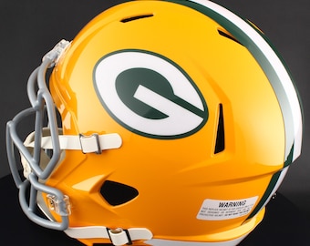 May include: A yellow football helmet with a green and white stripe and the Green Bay Packers logo. The helmet has a gray face mask and white chin straps. A warning label is visible on the side.