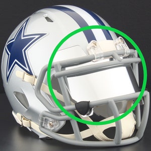 May include: Silver football helmet with a blue star logo and blue stripes. The helmet has a gray face mask and a clear visor. The straps are beige. The helmet is likely for a sports team.