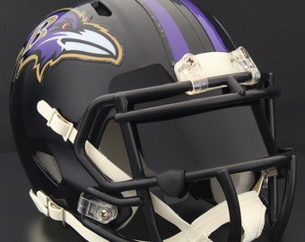 May include: A glossy black football helmet with a black facemask and white chin strap. The helmet features a purple and gold raven logo on the side and purple stripes on top.