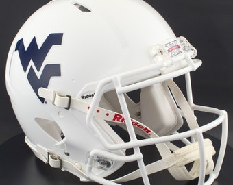 May include: White football helmet with a navy blue "WV" logo on the side. The helmet has a white face mask, chin strap, and a red and white Riddell strap. The helmet is designed for protection during football games.