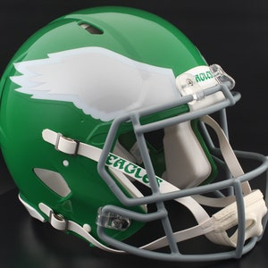 May include: A green football helmet with a white wing design on the side. The helmet has a gray face mask and a white chin strap. The word "EAGLES" is printed on the chin strap.