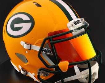 以下が含まれることがあります： グリーンベイ・パッカーズのアメリカンフットボールヘルメット。ヘルメットは黄色で、中央に緑と白のストライプがあり、側面に大きな緑色の「G」ロゴがあります。濃い緑色のフェイスマスクと赤色のバイザーが付いています。