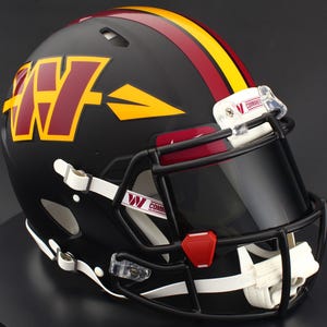 May include: A matte black football helmet featuring a burgundy and gold W logo with an arrow design on the side. The helmet has a black face mask, a tinted visor, and a central burgundy and gold stripe. White chin straps are attached to the sides.