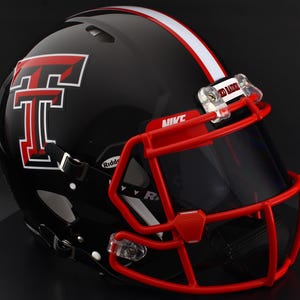 Puede incluir: Casco de fútbol americano negro con una máscara facial roja y una franja blanca. El casco presenta un gran logotipo "T" rojo y blanco y las palabras "Red Raiders" en el clip de la visera.