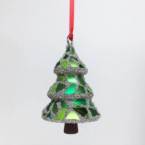 May include: A green and silver Christmas tree ornament with a red ribbon hanging from the top.