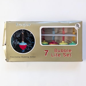 May include: A box of Everglow 7 Bubble Lite Set Christmas lights. The box is gold with a white border and features a picture of a single light bulb on a Christmas tree. The text on the box reads "Everglow", "Fascinating Bubbling Action", "7 Bubble Lite Set", and "UL".