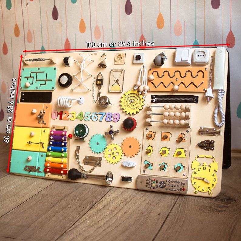 May include: A wooden activity board for toddlers with a variety of textures and activities, including a zipper, a lock, a clock, a xylophone, a bead maze, and a number puzzle. The board is 39.4 inches wide and 23.6 inches tall.