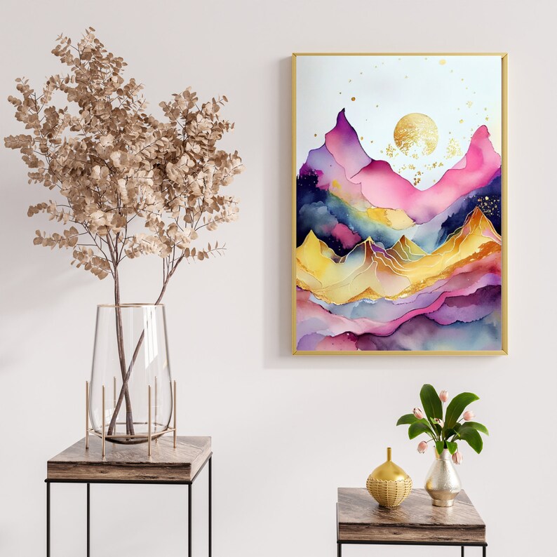 May include: Abstract watercolor painting of a mountain range with gold accents. The painting is in shades of pink, purple, blue, and yellow. The painting is framed in a gold frame and is hanging on a white wall.