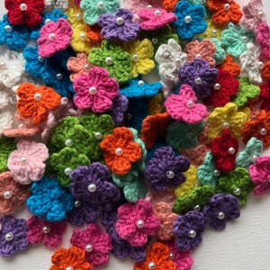 Pode incluir: Uma coleção de aplicações de flores de crochê coloridas em vários tons, incluindo rosa, laranja, verde, azul e roxo. Cada flor tem uma pérola branca no centro. Estas flores feitas à mão são adequadas para artesanato e embelezamento.
