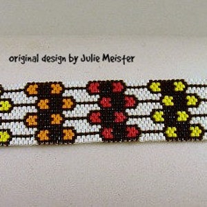 Puede incluir: Un brazalete blanco de cuentas con un patrón geométrico en rojo, naranja, amarillo y negro. El brazalete está hecho con pequeñas cuentas de semillas y tiene un diseño simple. "Original design by Julie Meister" está escrito en la superficie blanca detrás del brazalete.