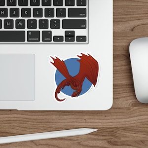 May include: Red dragon sticker with a blue circle background. The dragon is flying with its wings spread out and its tail curled.