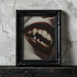 May include: A black framed picture with a close-up of a person's mouth with fangs and dark red lipstick.