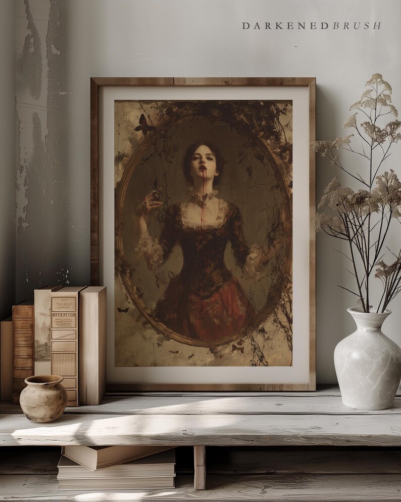 K&ouml;nnte beinhalten: Gerahmter Kunstdruck im Vintage-Stil mit einer Frau in einem dunklen Kleid mit Blut auf Gesicht und Hals. Das Kunstwerk befindet sich in einem ovalen Rahmen, umgeben von einem dekorativen Rand. Der Druck wird auf einem Holzregal mit B&uuml;chern und einer Vase ausgestellt.