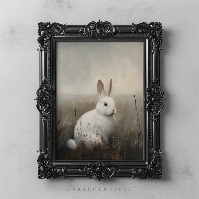 May include: A white rabbit sits in a field of tall grass, framed in a black ornate picture frame. The rabbit is facing the right side of the image, with its head tilted slightly down. The background is a soft, muted brown and gray, creating a dreamy atmosphere.