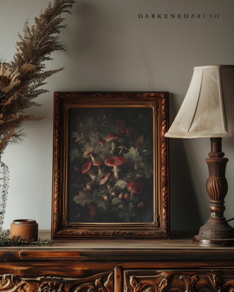 Op de afbeelding: Een ingelijst schilderij met rode paddenstoelen en bladeren, in een donkere, sfeervolle stijl. Het kunstwerk bevindt zich in een sierlijke gouden lijst. De tekst "DARKENDEDBRUSH" staat boven het frame. De schilderij staat op een houten oppervlak.